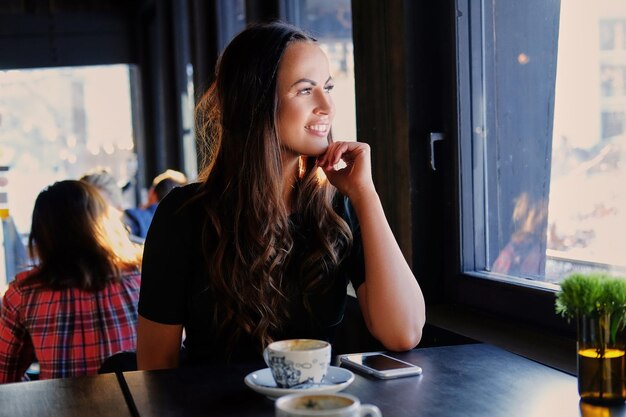 笑顔のブルネットの女性の肖像画は、カフェで朝のコーヒーを飲みます。