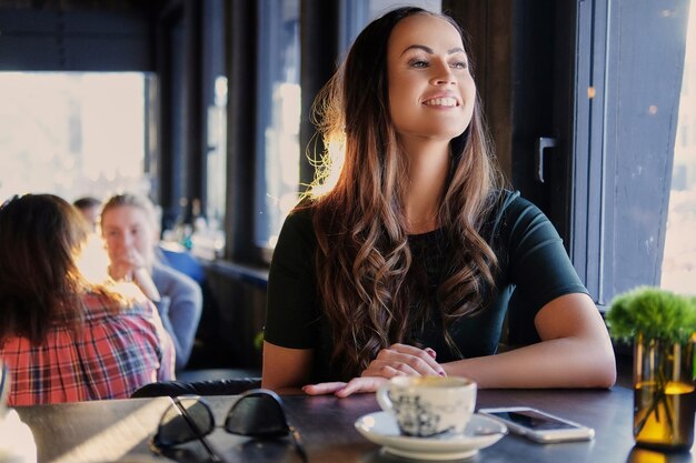 笑顔のブルネットの女性の肖像画は、カフェで朝のコーヒーを飲みます。