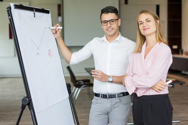 Portrait of smiling business colleagues drawing plan on flip chart. 