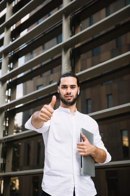 Portrait of a smiling businessman holding laptop in hand showing thumb up sign