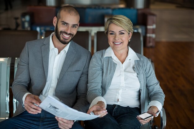 Portrait of smiling businesspeople sitting in waiting area with newspaper