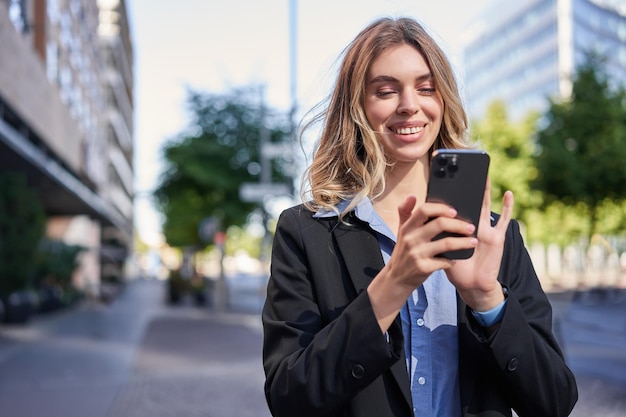 Портрет улыбающейся деловой женщины, использующей мобильный телефон, стоя на улице возле офисных зданий