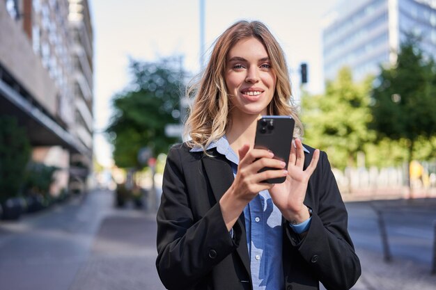 Portrait of smiling businesswoman using mobile phone while standing outdoors near office buildings