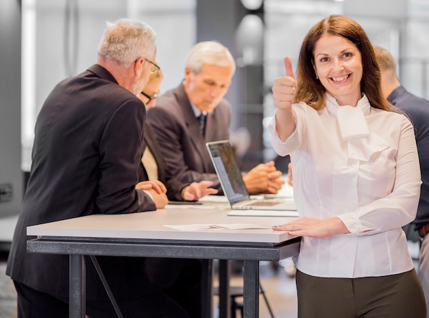 Free photo portrait of smiling businesswoman at workplace showing thumb up sign