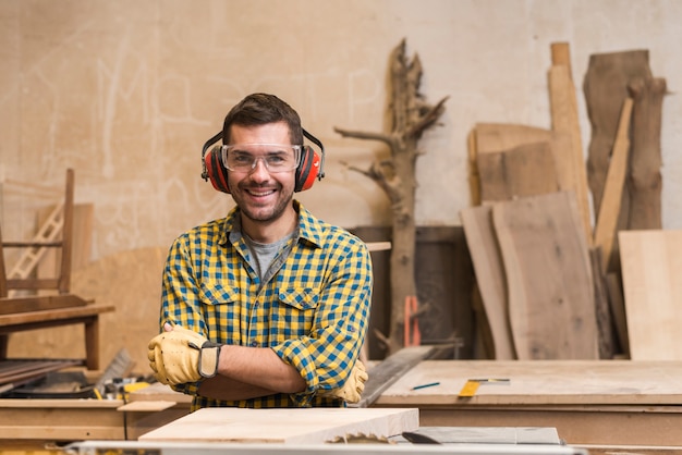 Портрет улыбающегося плотника в защитных очках и защитника в мастерской