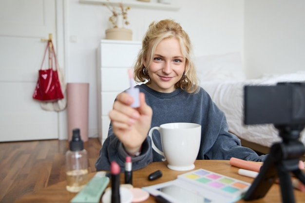 Foto gratuita ritratto di una donna sorridente e carismatica che si mette il lucido per le labbra, beve tè e registra video con una telecamera digitale