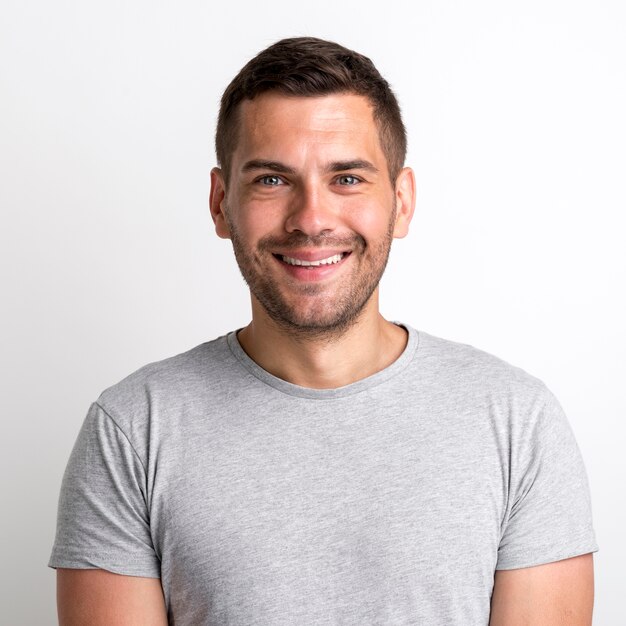 Портрет улыбающегося очаровательного молодого человека в серой футболке, стоящего на простом фоне