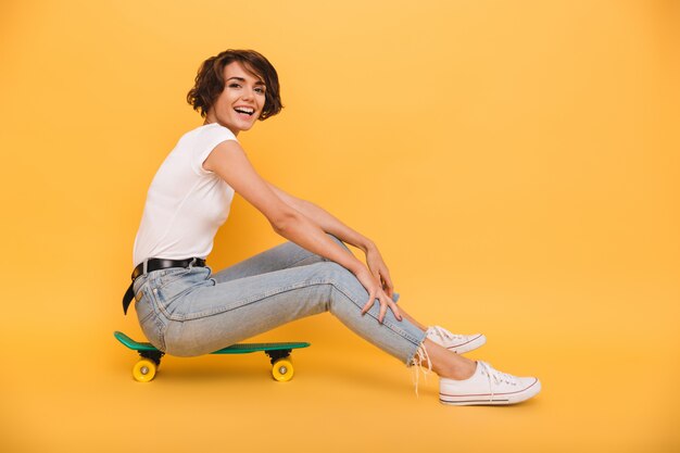 Portrait of a smiling cheerful woman sitting on a skateboard