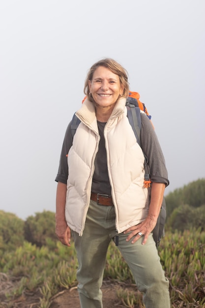 Portrait of smiling elderly woman with backpack. Sporty woman in casual clothes looking at camera with bright smile. Sport, adventure, hobby concept