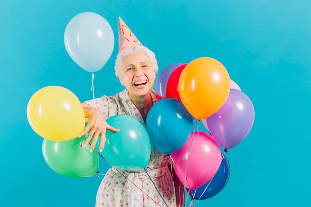 Портрет улыбающейся пожилой женщины с красочными воздушными шарами на синем фоне