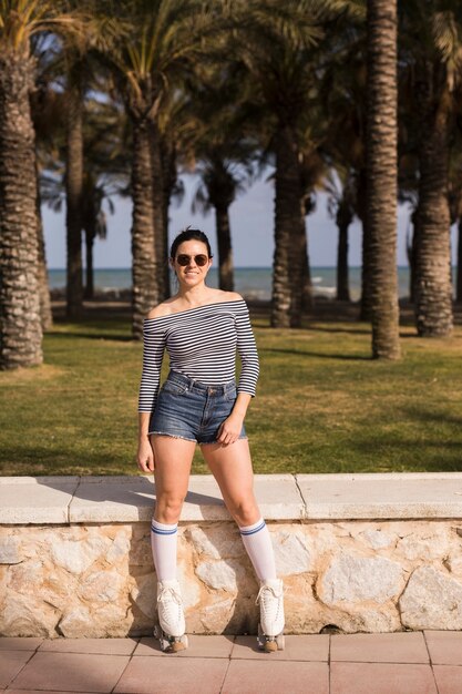 Portrait of a smiling fashionable young female skater standing in front of trees