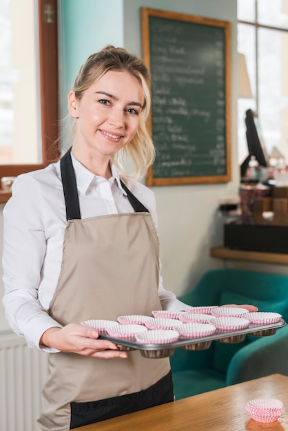 Portrait of a smiling female baker holding muffins baking tray