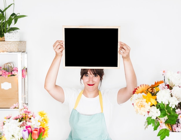 Portrait of a smiling female florist holding blank slate near fresh flowers