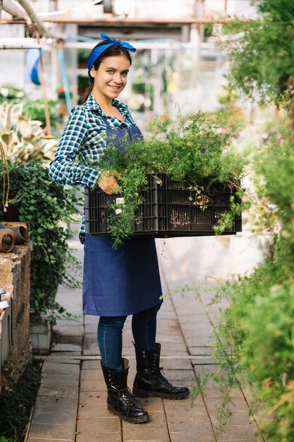 Portrait of a smiling female gardener holding crate with fresh plants