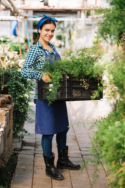 新鮮な植物と木箱を保持している笑顔の女性庭師の肖像