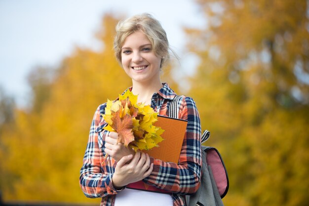 Портрет улыбается женщина молодых студентов на открытом воздухе, холдинг желтые листья