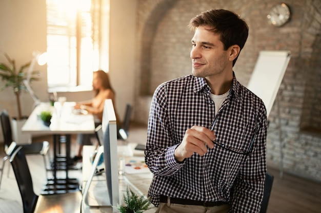 Ritratto di lavoratore freelance sorridente che distoglie lo sguardo stando in piedi in ufficio