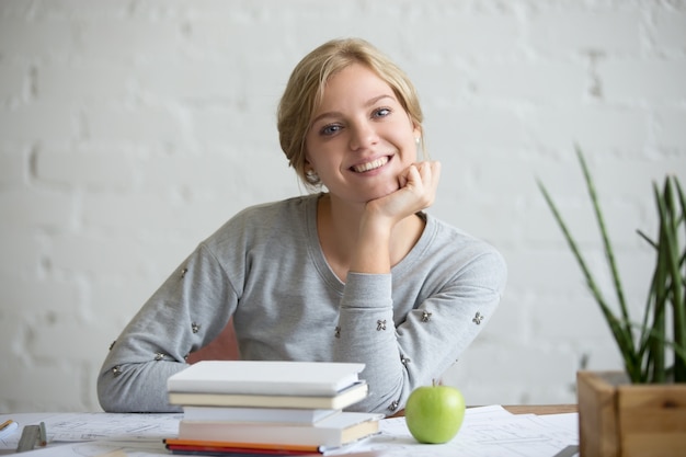 Ritratto di ragazza sorridente alla scrivania con libri e mela