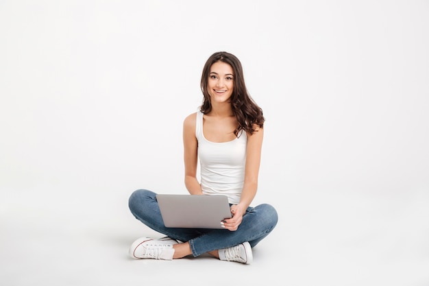 Portrait of a smiling girl dressed in tank-top holding laptop