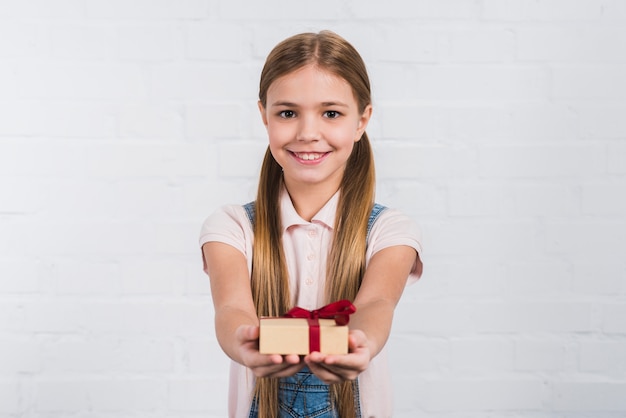 Portrait of a smiling girl giving wrapped present against white background