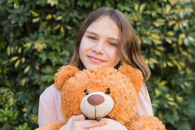 Portrait of a smiling girl holding teddy bear at outdoors