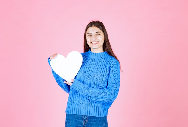 Portrait of smiling girl holding white heart isolated on pink.