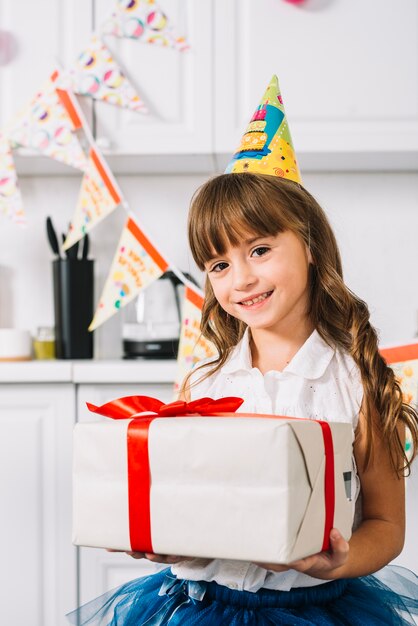 Portrait of a smiling girl holding white wrapped gift box tied with red ribbon on her birthday