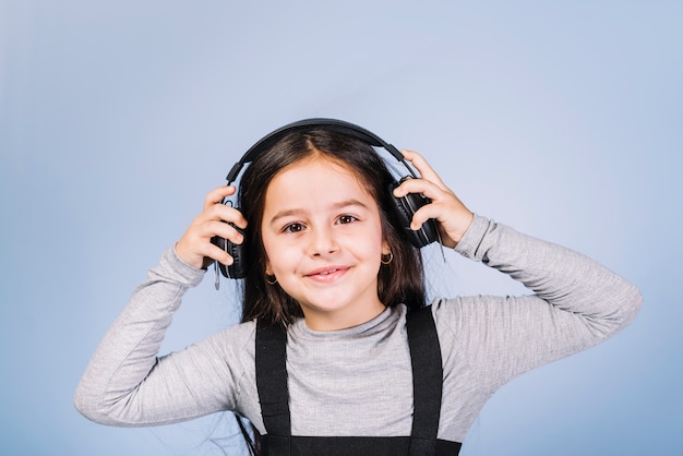 Portrait of a smiling girl listening music on headphone against blue backdrop