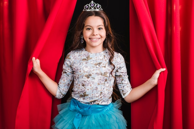 Free photo portrait of smiling girl looking out from red curtain