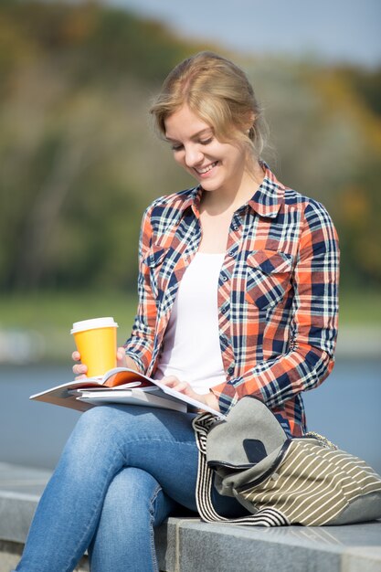 Free photo portrait of a smiling girl sitting at the bridge reading