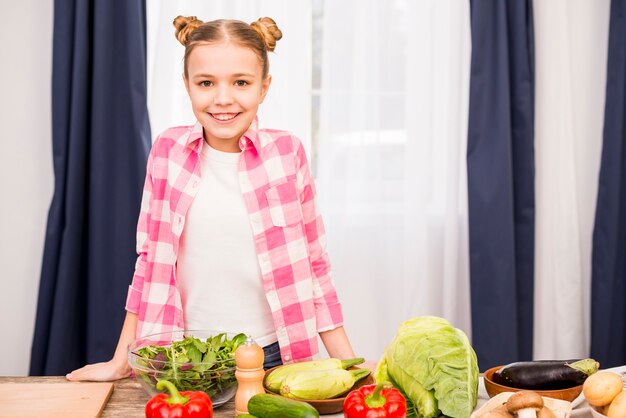 新鮮な野菜とテーブルの後ろに立っている微笑の女の子の肖像画