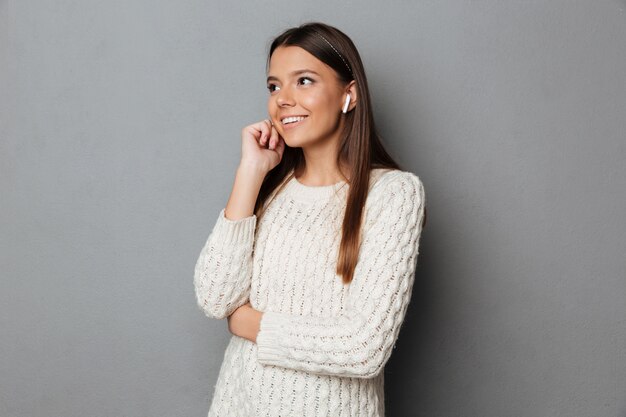 Portrait of a smiling girl in sweater using wireless earphones