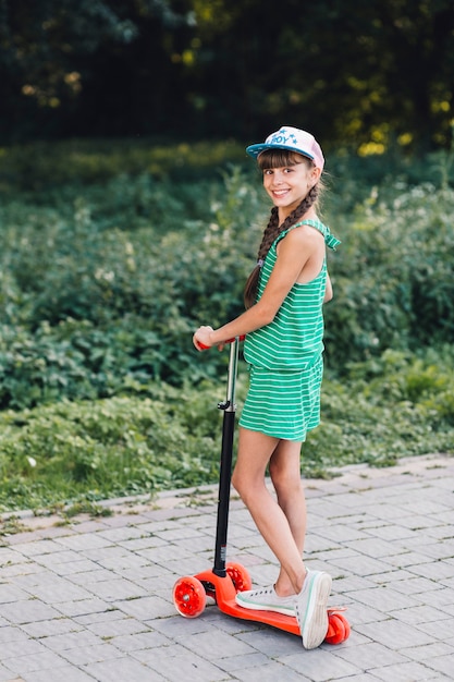 Portrait of smiling girl wearing cap standing on scooter