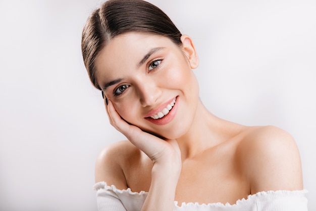 Portrait of smiling girl with healthy skin. Cute dark-haired woman on white wall.