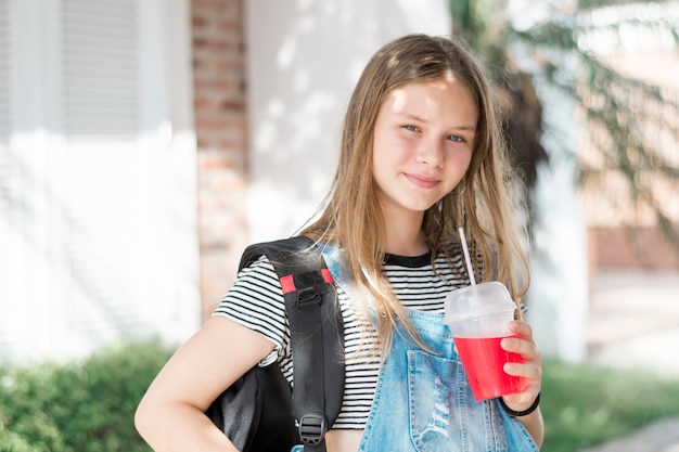 Free photo portrait of smiling gorgeous girl looking at camera with holding cold drink and bag