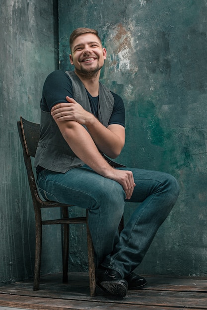 Portrait of smiling happy man sitting on the wooden chair on gray studio