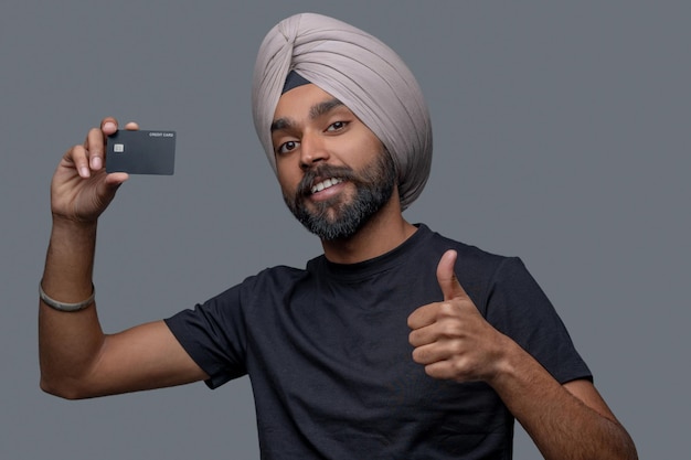 Portrait of a smiling happy man with a credit card in his hand making a thumbs-up gesture