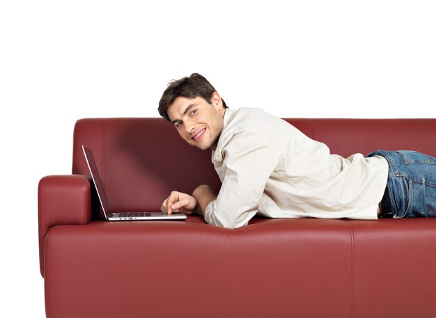 Portrait of smiling happy man with laptop on divan, isolated on white. 
