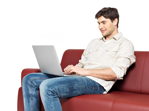 노트북과 웃는 행복 한 남자의 초상화는 흰색 절연 긴의 자에 앉아있다.