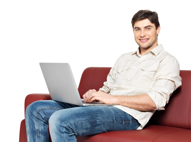 Portrait of smiling happy man with laptop sits on divan, isolated on white. 
