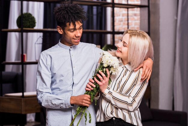 portrait of smiling interracial young couple holding white flower bouquet