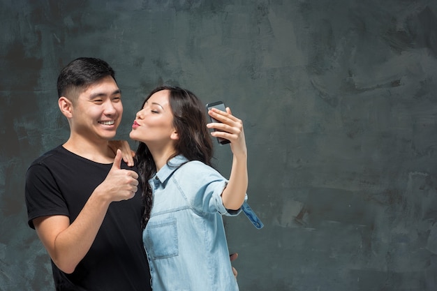 灰色のスタジオの背景にselfie写真を作る韓国のカップルを笑顔の肖像画