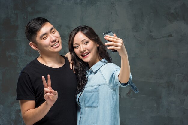 Портрет улыбающейся корейской пары, делающей селфи-фото в серой студии