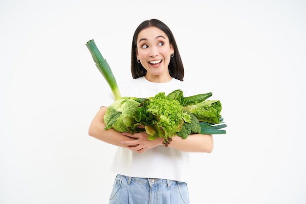 Portrait of smiling korean woman hugs her vegetables likes eating raw food vegetarian enjoys nutriti