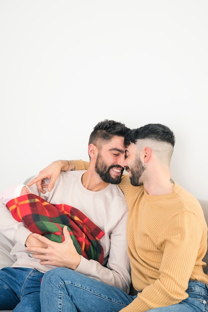 Free photo portrait of smiling loving gay couple with their baby in hand isolated against white backdrop