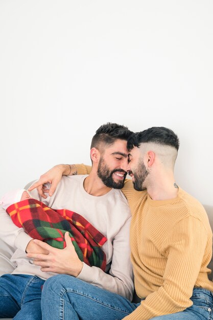 Portrait of smiling loving gay couple with their baby in hand isolated against white backdrop