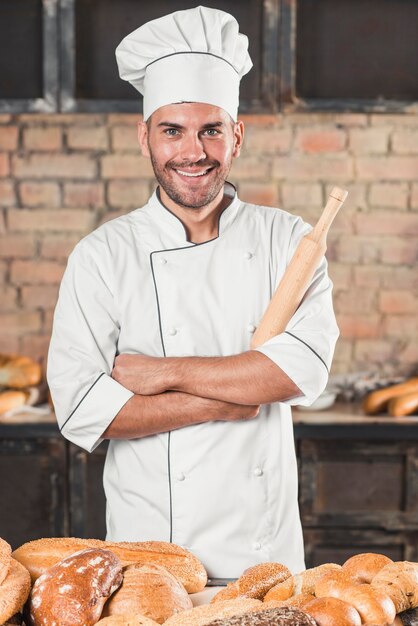 Portrait of smiling male baker standing behind the breads on table