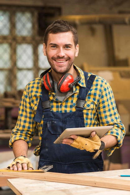 Portrait of a smiling male carpenter holding digital tablet in hand looking at camera