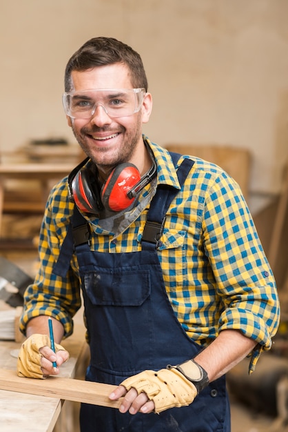 木製の厚板と鉛筆を持っている笑顔の男性の大工の肖像