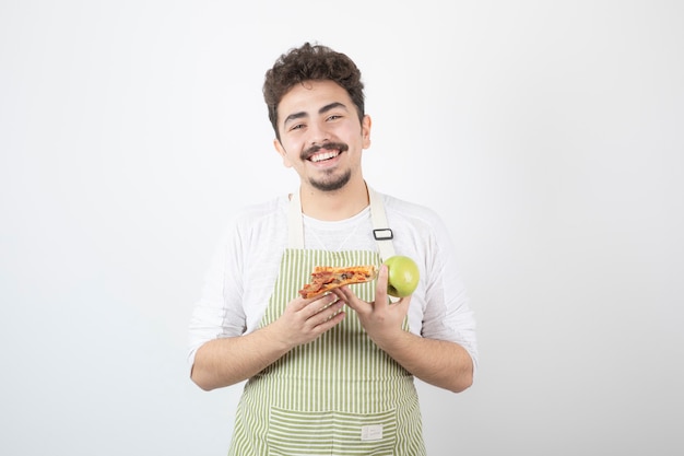 Free photo portrait of smiling male cook holding apple and pizza on white